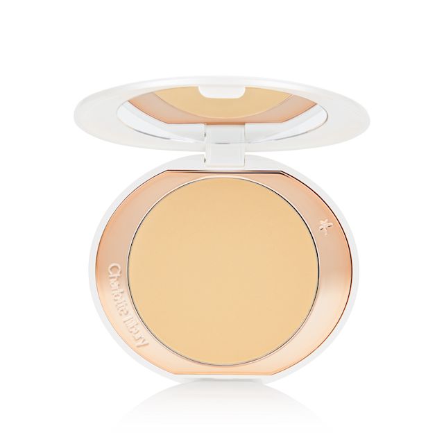 An open, setting powder compact in banana-yellow with a mirrored-lid and white and gold-coloured packaging.
