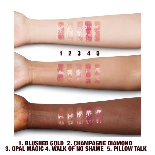 Fair, tan, and deep-tone arms with swatches of five shimmery lip glosses in shades of pink, champagne, peach, and gold. 
