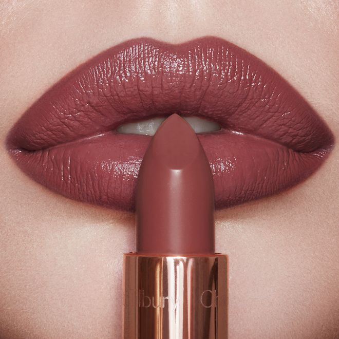 K.I.S.S.I.N.G. in Pillow Talk Intense light-skin model lips close-up Lips close-up of a light-tone model wearing a dark, brown-pink lipstick with a satin finish while holding the lipstick in front of her.