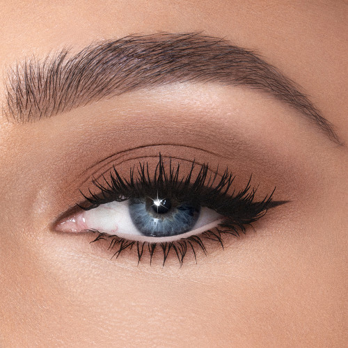 Single-eye close-up of a fair-tone model with blue eyes wearing chocolate brown cream eyeshadow smudged and spread on her eyelid with black eyeliner for a smokey brown eye look. 
