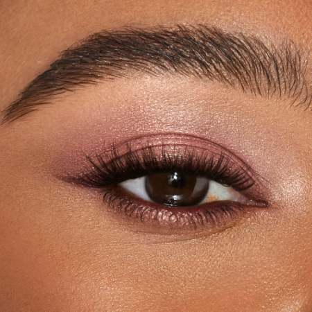 Single-eye close-up of a deep-tone model with brown eyes wearing shimmery rose gold eyeshadow.