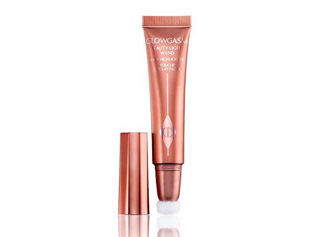An open highlighter wand in a warm pink shade, in rose gold packaging with its lid next to it. 
