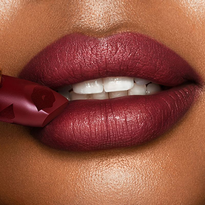 Lips close-up of a deep-tone model wearing a winter berry matte lipstick while holding the lipstick against her lips.