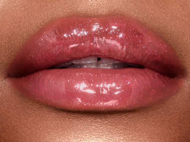 Lips close-up of a deep-tone model wearing shimmery berry-pink lip gloss. 
