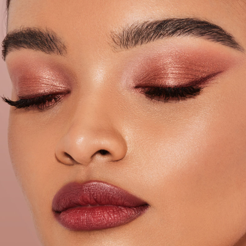 Close-up of a medium-tone model wearing cream eyeshadows in dusty pink with rose-gold sparkle and russet-rose with golden-peach glimmer along with berry-red lipstick. 