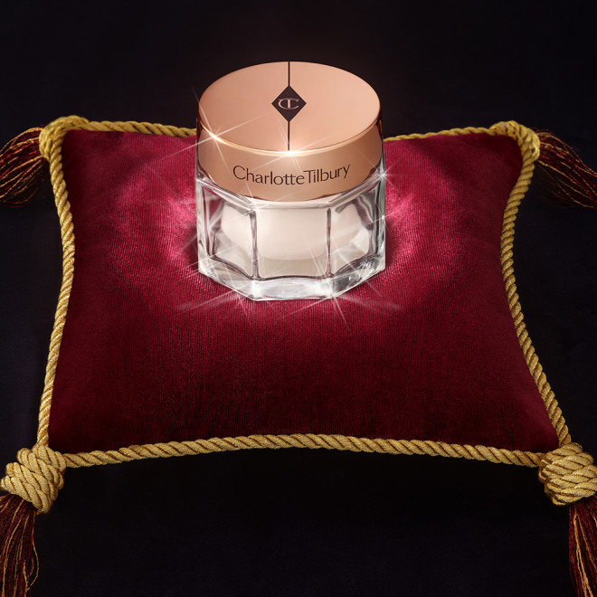 Pearly-white face cream in a glass jar with a gold-coloured lid on a red velvet cushion. 