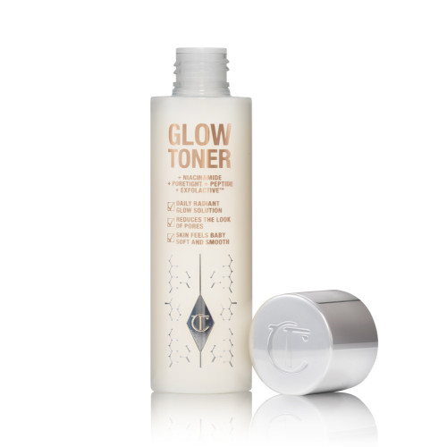 An open, large, clear bottle filled with luminous, cream-coloured watery toner with its silver-coloured lid next to it.