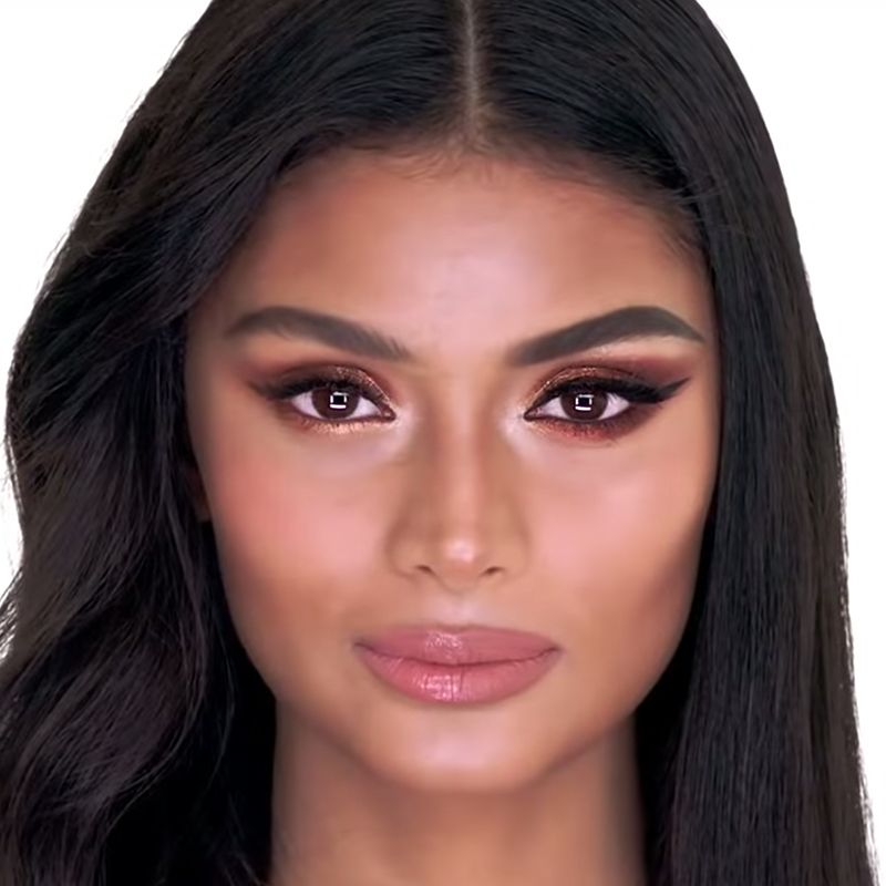 A medium-tone model with brown eyes wearing an Instagram-inspired bold and glamorous look on one side of her face and a soft-glam makeup look on the other half. 