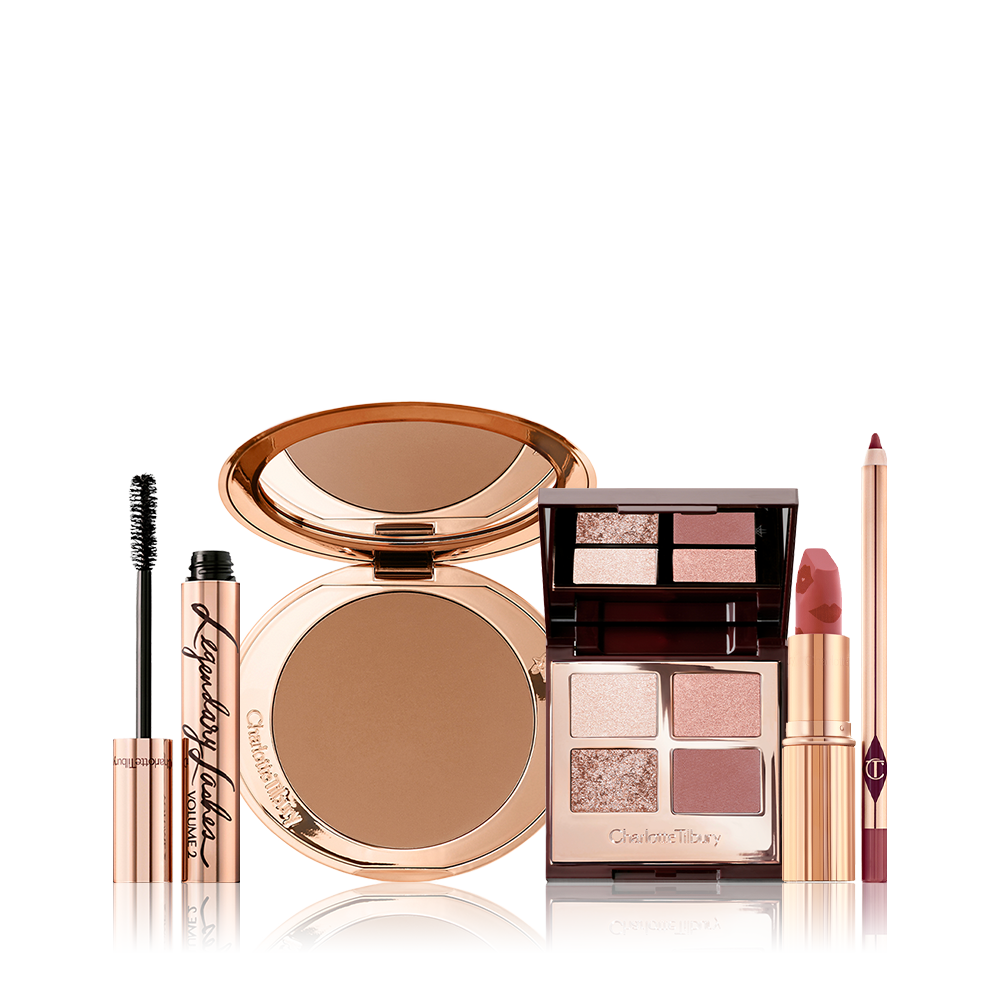 An open bronzer compact, open lipstick in a golden peachy-pink shade, quad eyeshadow palette with ivory-cream, rose-gold, red-brown and transparent sparkle shades, open mascara, and a deep nude pink lip liner pencil.  