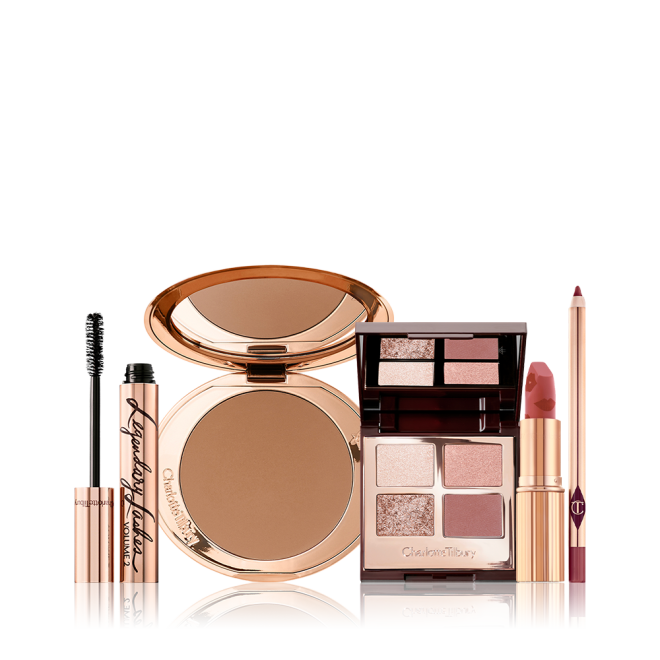 An open bronzer compact, open lipstick in a golden peachy-pink shade, quad eyeshadow palette with ivory-cream, rose-gold, red-brown and transparent sparkle shades, open mascara, and a deep nude pink lip liner pencil.  