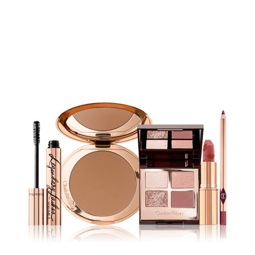 An open bronzer compact, open lipstick in a golden peachy-pink shade, quad eyeshadow palette with ivory-cream, rose-gold, red-brown and transparent sparkle shades, open mascara, and a deep nude pink lip liner pencil.  
