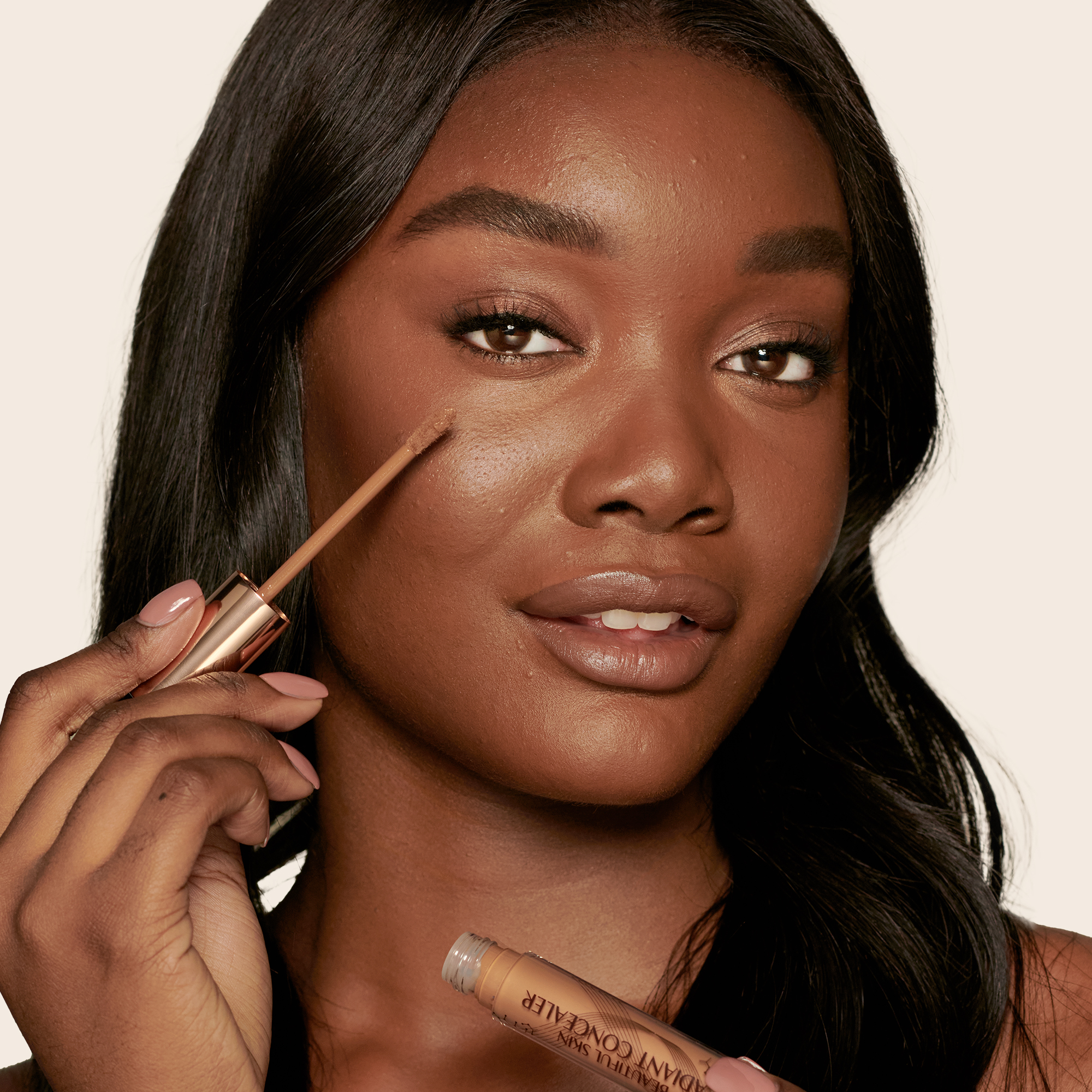 Deep-tone model with brown eyes wearing a radiant, concealer that brightens, covers blemishes, and makes her skin look fresh along with nude lip gloss and subtle eye makeup.