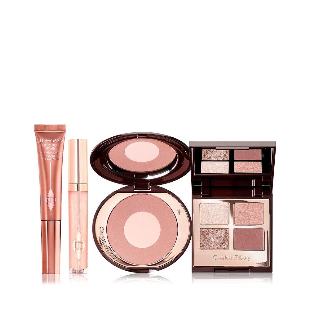 An open two-tone blush compact in nude pink and champagne, open mirrored-lid eyeshadow palette in neutral gem shades, sheer pink lip gloss, and bronze-gold-coloured liquid highlighter wand. 