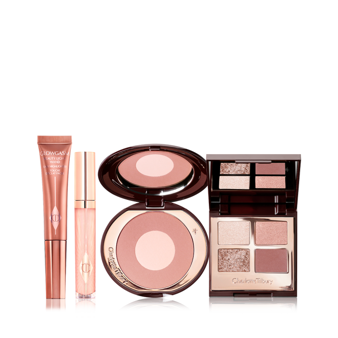 An open two-tone blush compact in nude pink and champagne, open mirrored-lid eyeshadow palette in neutral gem shades, sheer pink lip gloss, and bronze-gold-coloured liquid highlighter wand. 