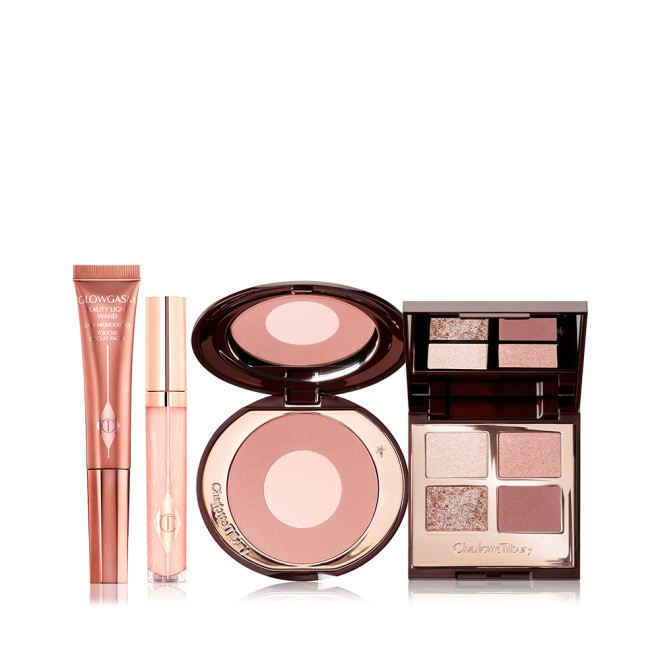 An open two-tone blush compact in nude pink and champagne, open mirrored-lid eyeshadow palette in neutral gem shades, sheer pink lip gloss, and bronze-gold-coloured liquid highlighter wand. 