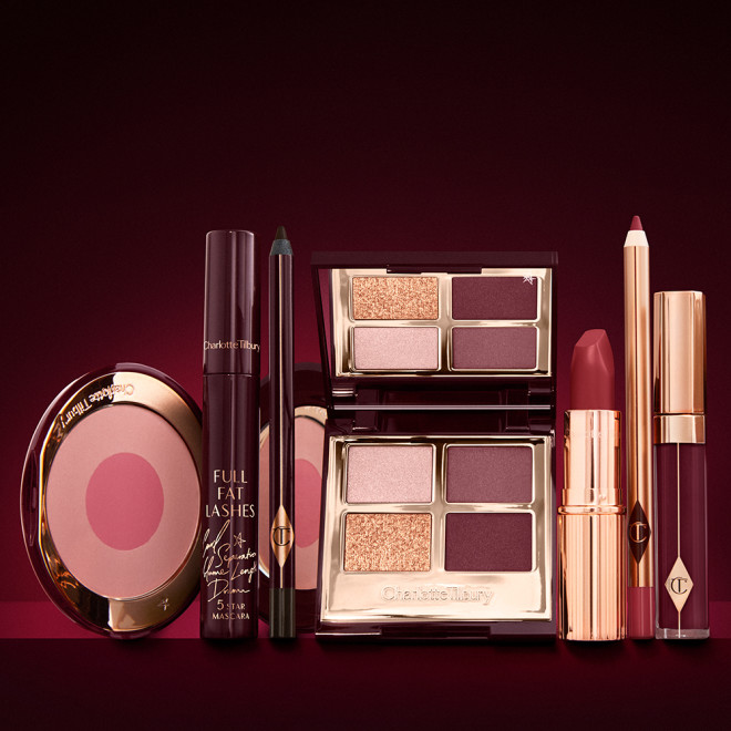 An open, mirrored-lid eyeshadow palette in matte and shimmery gold and red shades, an open black eyeliner pencil, a mascara in a dark-crimson colour scheme, a red lipstick with a matching lip liner pencil, vampy-red lip gloss, and an open two-tone blush in cool pink. 