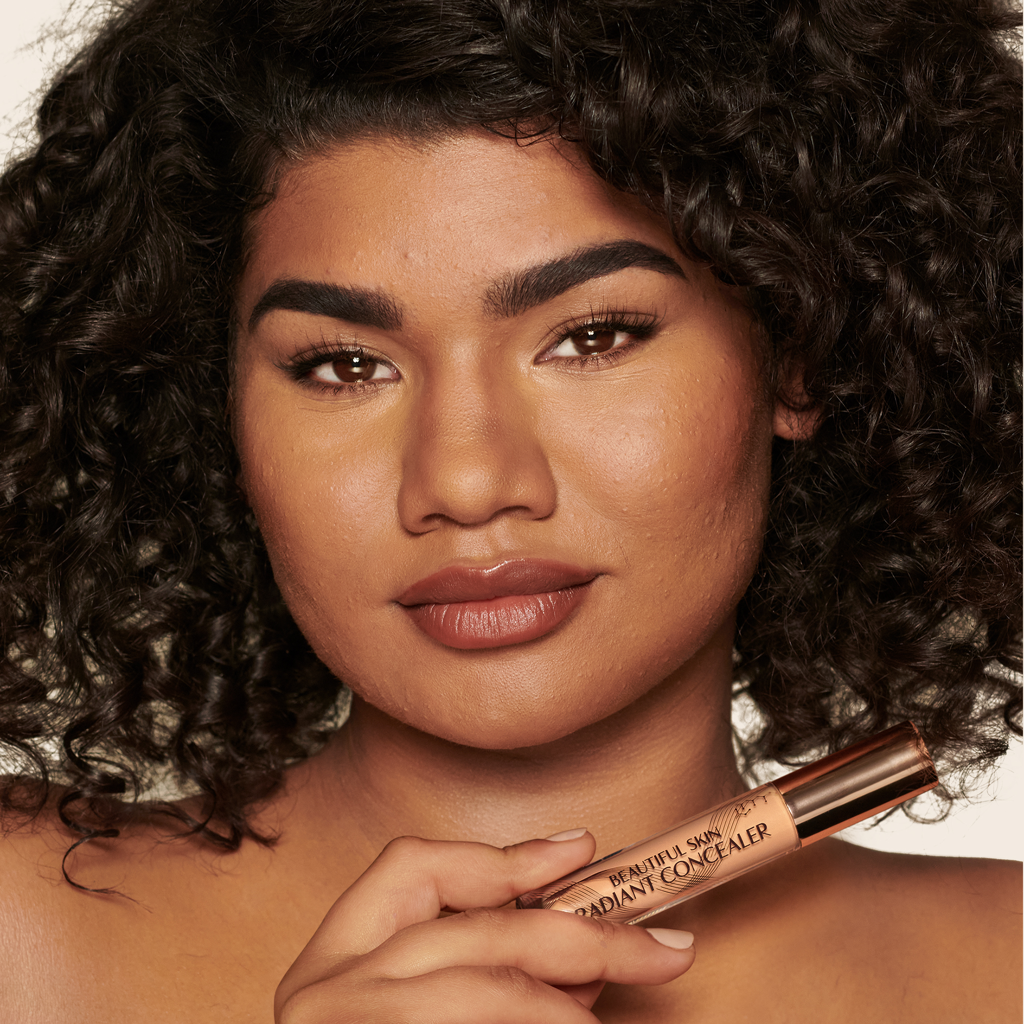 Deep-tone model with brown eyes wearing a radiant, concealer that brightens, covers blemishes, and makes her skin look fresh along with nude lip gloss and subtle eye makeup.
