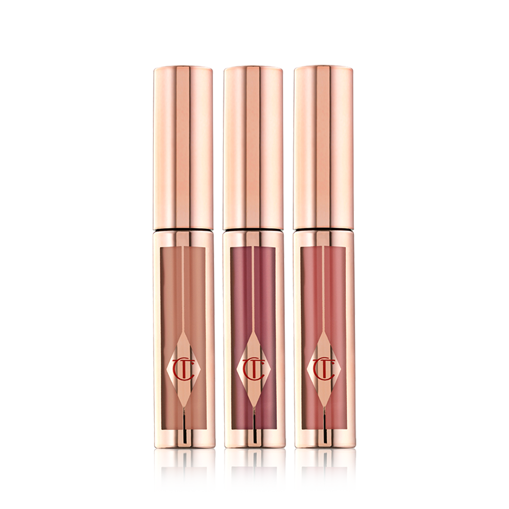 A trio of liquid lipsticks in clear tubes with gold-coloured lids in shades of light brown, muted purple wine, and nude pink. 