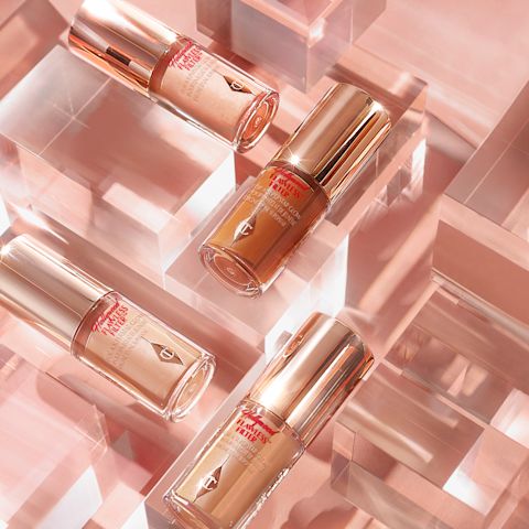 A collection of mini, glowy primers in fair, medium, and deep shades in glass bottles with gold-coloured lids placed on a glass maze-like table.