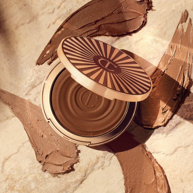 Open, cream bronzer compact in a dark-brown shade with gold-coloured packaging with swatches of four bronzers in light and dark brown shades beneath it. 