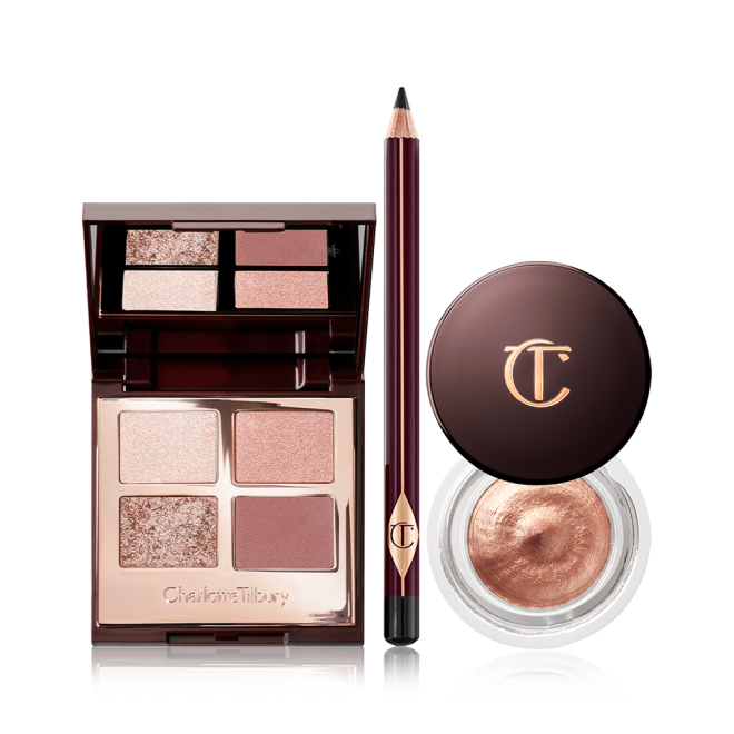 An open, mirrored-lid quad eyeshadow palette with beige, brown-gold, rose gold, and dusky pink shades, an eyeliner pencil in black, and cream eyeshadow in a coppery-gold shade in a glass pot with a dark brown-coloured lid. 