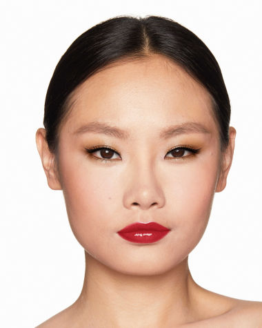 A fair-tone model with brown eyes wearing shimmery bronze eye makeup with muted pink blush and glossy scarlet-red lips