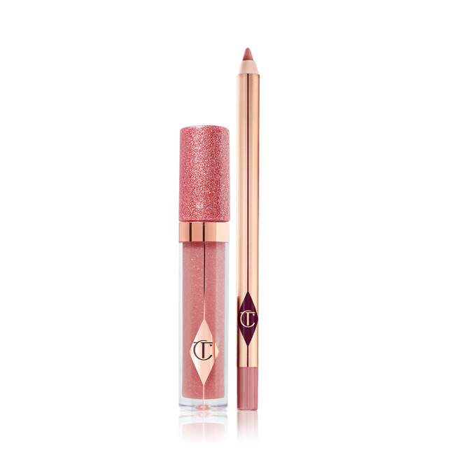 Shimmery lip gloss in a nude pink shade in a glass tube with a glittery lid with an open lip liner pencil in a nude pink shade. 