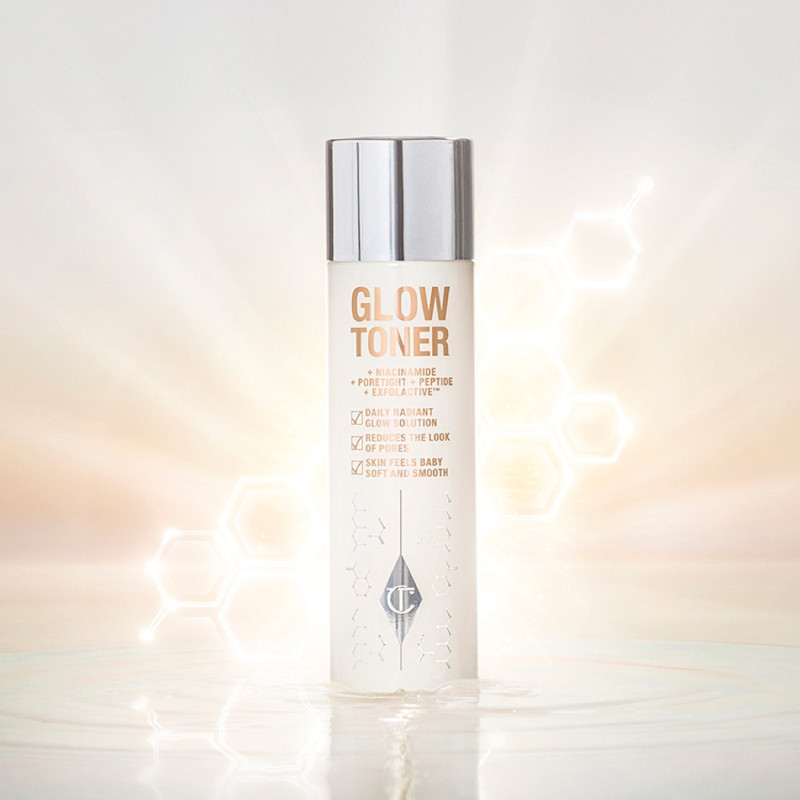 Un grand flacon transparent rempli d’une lotion tonique aqueuse, lumineuse et de couleur crème, avec un bouchon argenté.