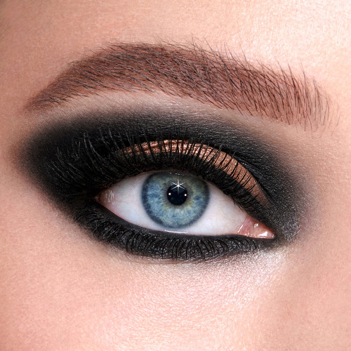Single-eye close-up of a fair-tone model with blue eyes wearing smokey black and fawn eyeshadow with black kohl liner to create a sultry, dark, smokey look.