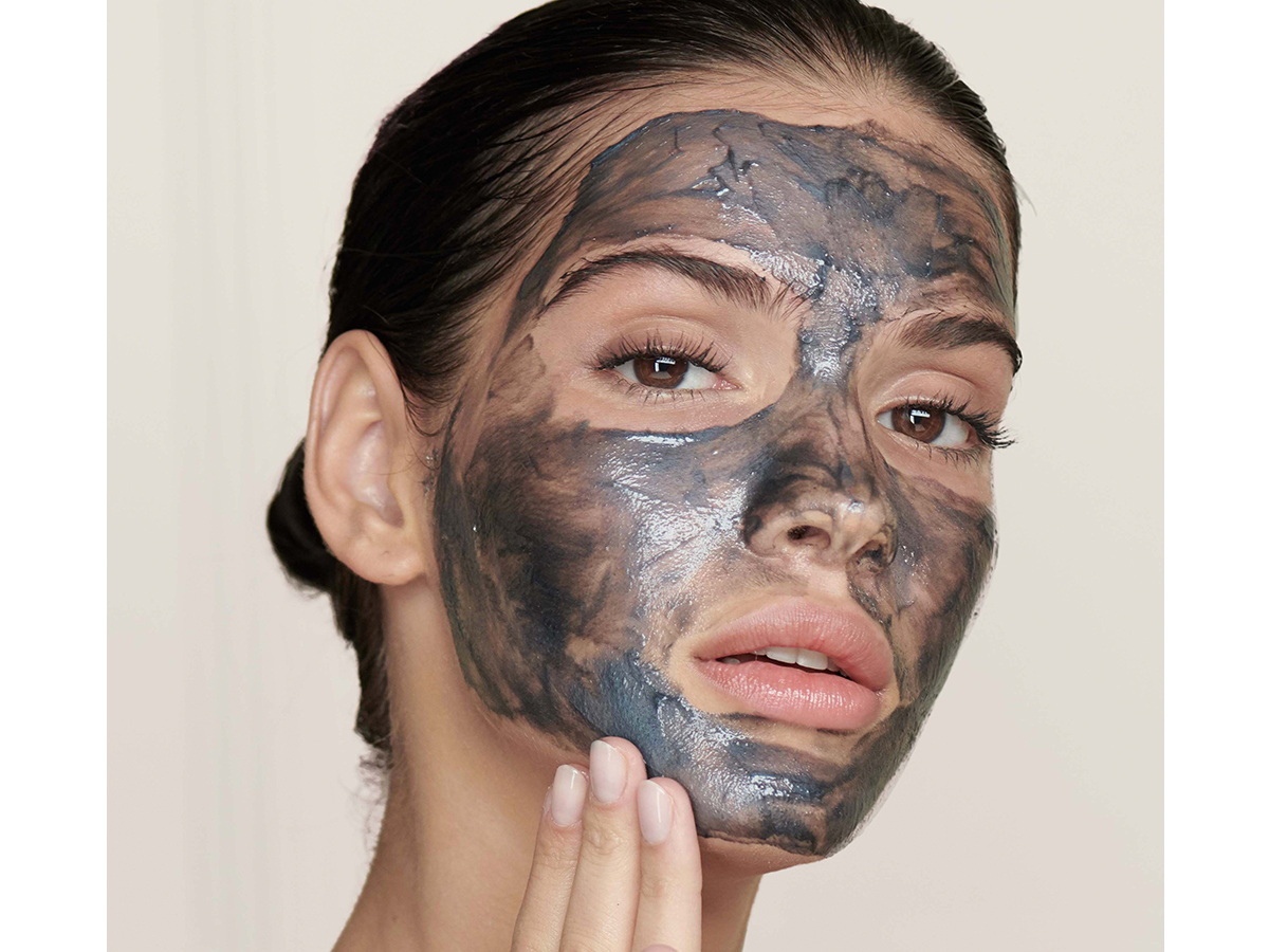 A light-tone brunette model applying a charcoal cleanser on her face.