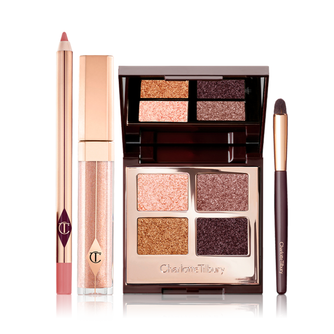 A nude pink lip liner pencil, liquid lipstick in a nude fawn shade in gold coloured packaging, an eyeshadow smudger brush, and an open, quad eyeshadow palette with a mirrored-lid with four shimmery eyeshadows in shades of gold, pink, and grey.