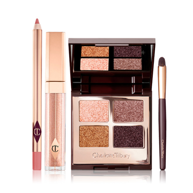 A nude pink lip liner pencil, liquid lipstick in a nude fawn shade in gold coloured packaging, an eyeshadow smudger brush, and an open, quad eyeshadow palette with a mirrored-lid with four shimmery eyeshadows in shades of gold, pink, and grey.