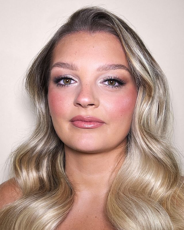 Close-up of a fair-tone model with green eyes wearing soft pinkish-peach matte lipstick with reddish-pink blush, and brown and beige eye makeup.