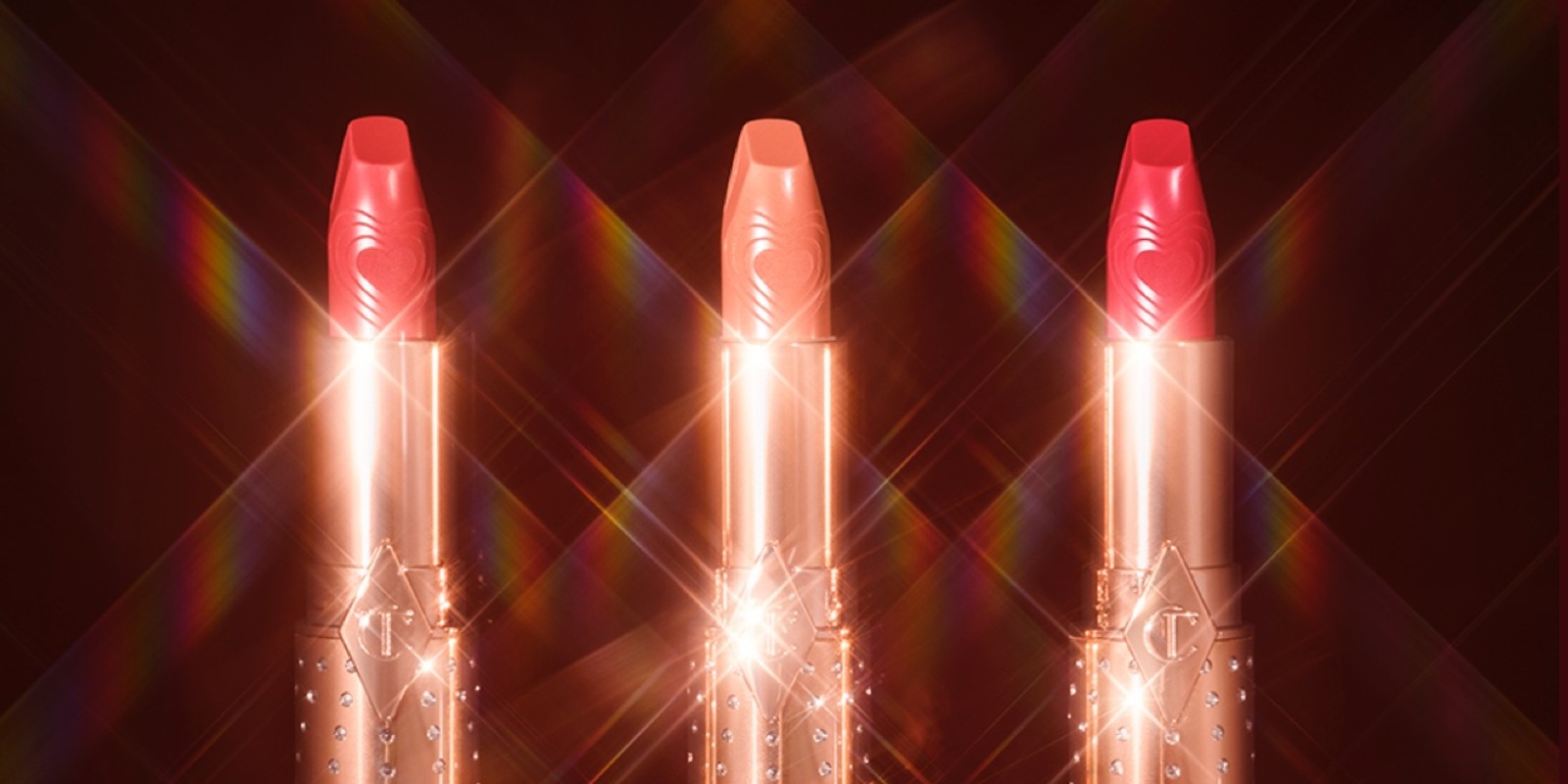 Three open lipsticks in shades of nude pink, gold peach, and bright pink in gold-coloured tubes with sparkles all over.