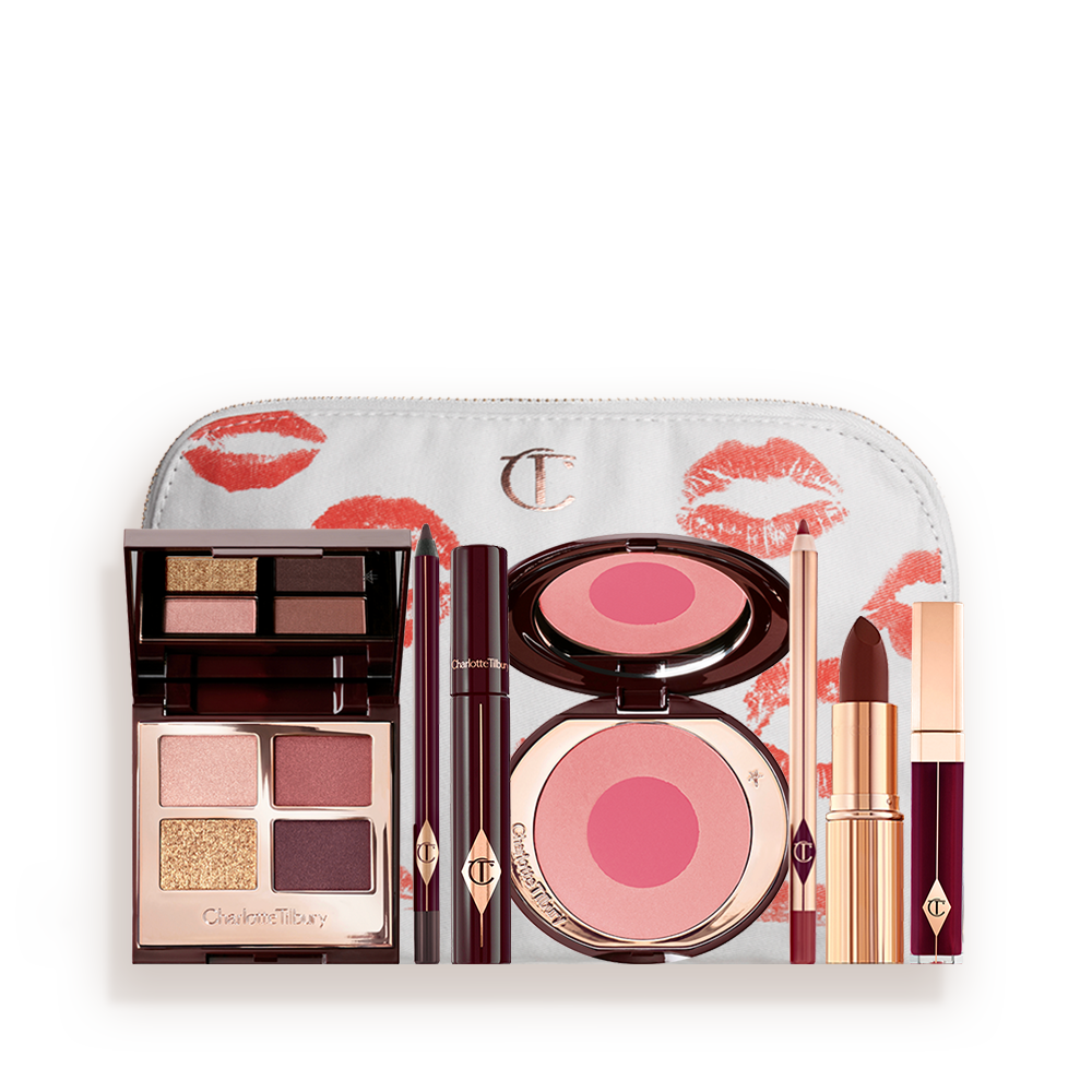 A makeup bag with 7 makeup products, which are a quad eyeshadow palette in shades of champagne, gold, and berry, a dark brown eyeliner pencil, mascara, a two-tone peal pink powder blush, burgundy lip liner, a reddish-plum lipstick, and a reddish-plum lip gloss. 