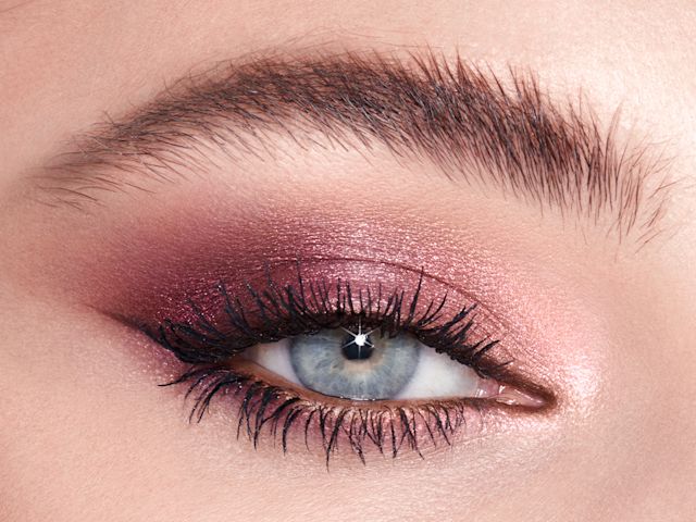 Single-eye close-up of a fair-tone model with blue eyes wearing shimmery rose gold and purple eyeshadow. 