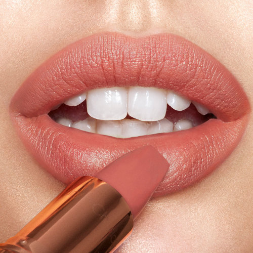 Lips close-up of a light-tone model applying a nude pinky peach lipstick. 