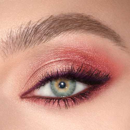Close-up of a shimmery, peach, plum, and champagne eye look on a fair-tone model with green eyes. 