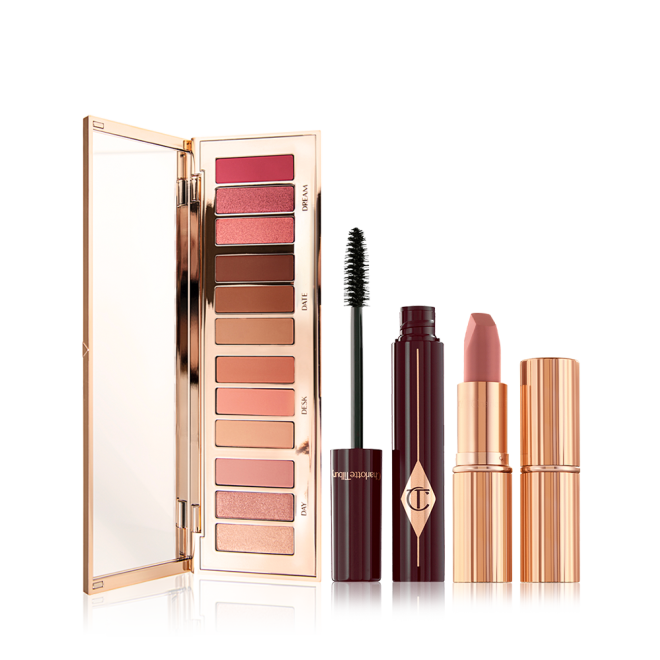 An open, mirrored-lid eyeshadow palette with nude pink, peach, and brown shades, an open mascara with its applicator next to it, and an open nude pink lipstick with a closed lipstick. 