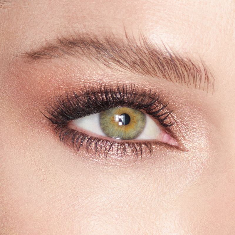 Single-eye close-up of a model with green eyes wearing cream eyeshadow in an antique oyster-gold shade.