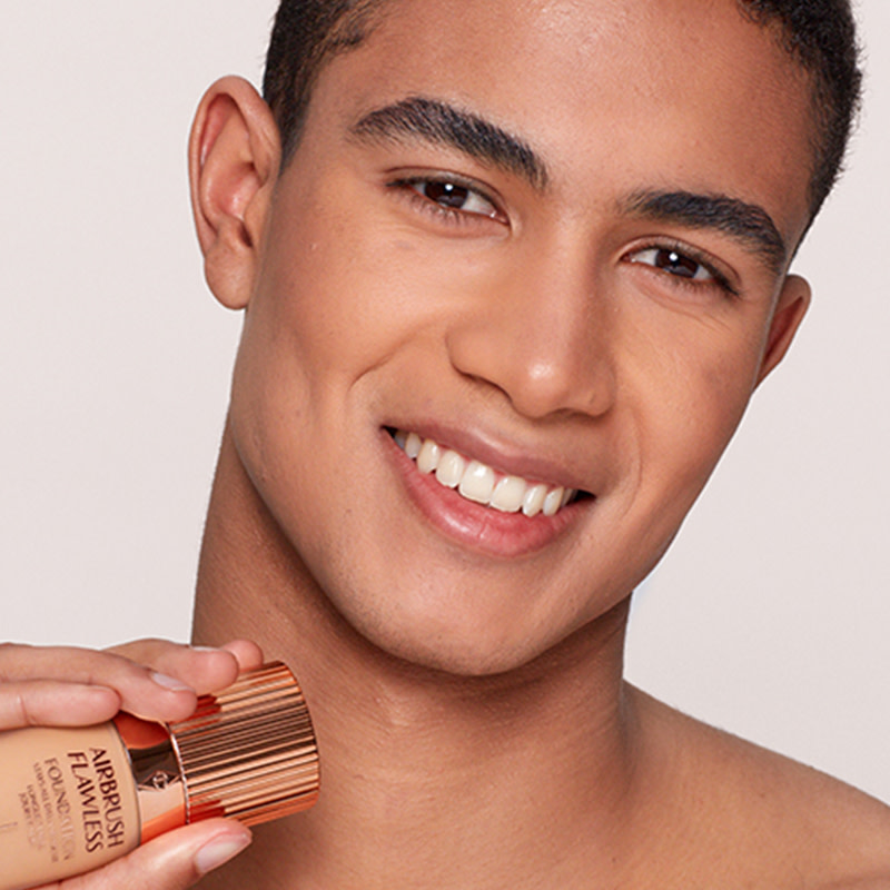 A deep-tone, brunet male model wearing dewy, natural-looking makeup. 