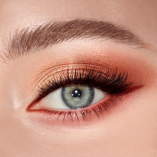 Single-eye close-up of a fair-tone model with blue eyes wearing shimmery copper, peach, and gold eye makeup.