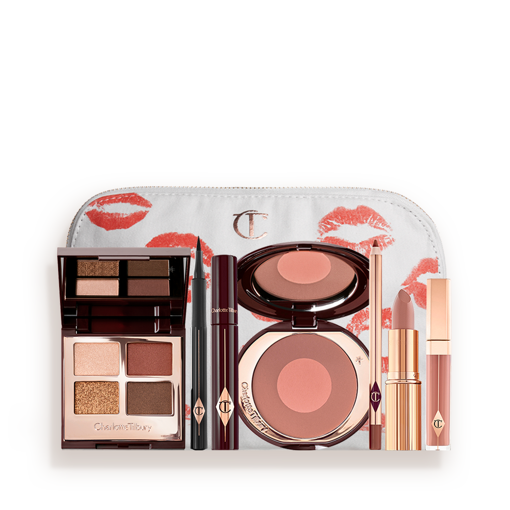 A white makeup pouch with an open two-tone blush in cool-toned brown and warm pink with a mascara, eyeliner pen, quad eyeshadow palette with shimmery and matte brown and golden shades, an open lipstick in nude peach, lip liner pencil in taupe-brown, and a lip gloss in nude pink. 