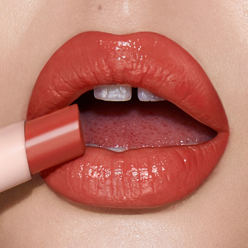 Lips close-up of a light-tone model wearing a glossy soft coral lipstick lip balm. 