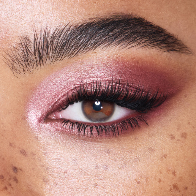Single-eye close-up of a light-tone model with brown eyes wearing metallic pink-purple eye makeup with black eyeliner.