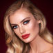A fair-tone model with blue eyes wearing shimmery bronze eye makeup with muted pink blush and glossy scarlet-red lips
