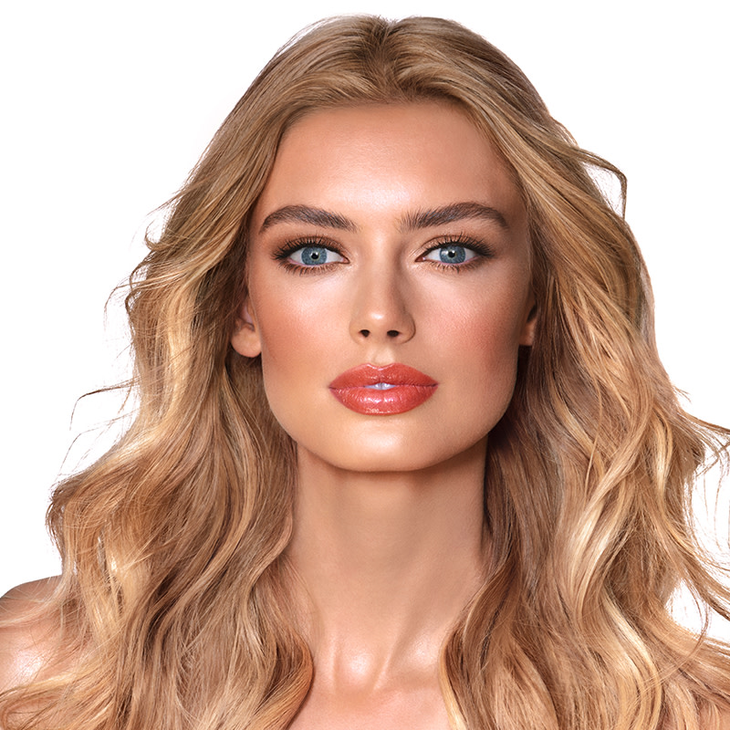 A light-tone model with blue eyes wearing smokey brown eye makeup with warm bronze and pink blush, and glossy terracotta lips.