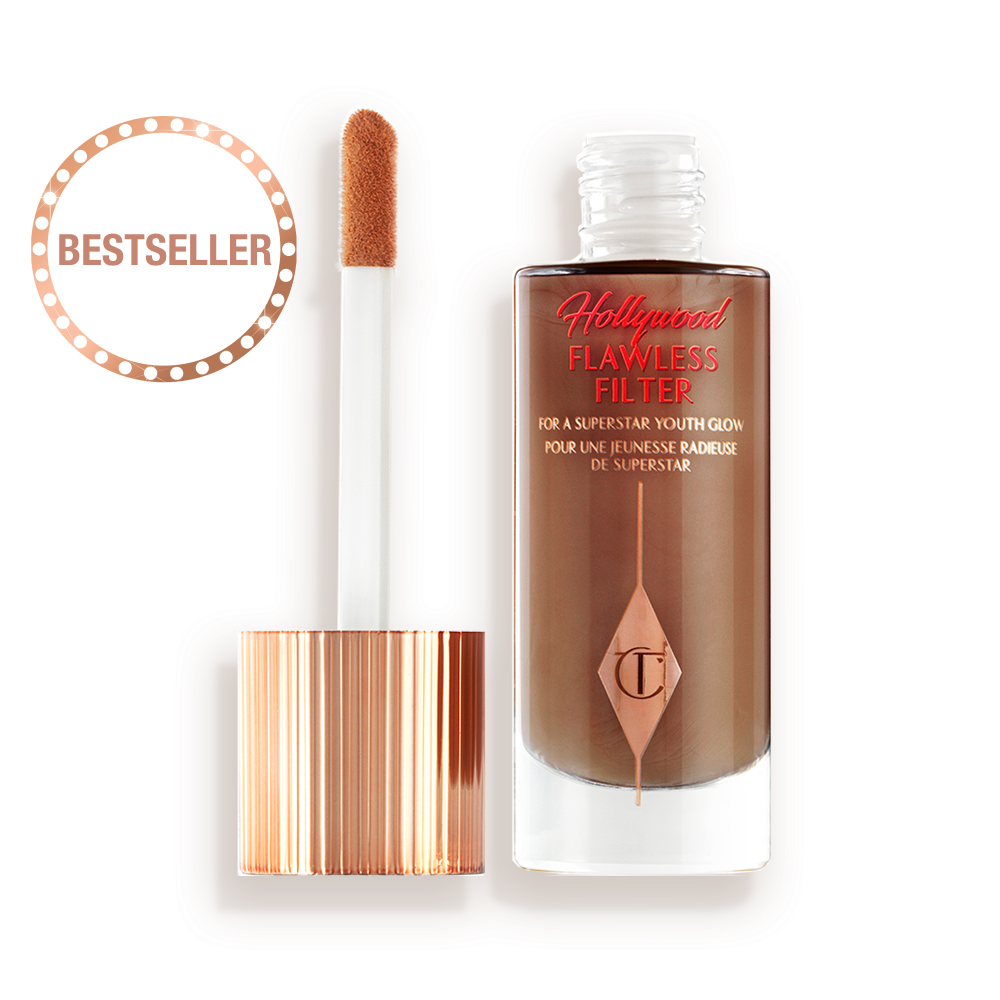 An open, luminous primer in a dark brown shade in a glass bottle with its gold and white doe-foot applicator next to it.