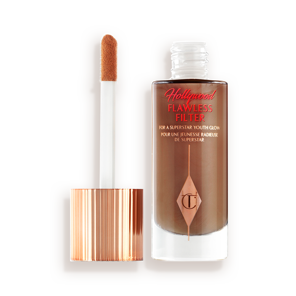 Ein leuchtender Primer in einem dunkelbraunem Farbton in einer geöffneten Glasflasche mit seinem angeschrägten Applikator in Gold und Weiß neben sich.