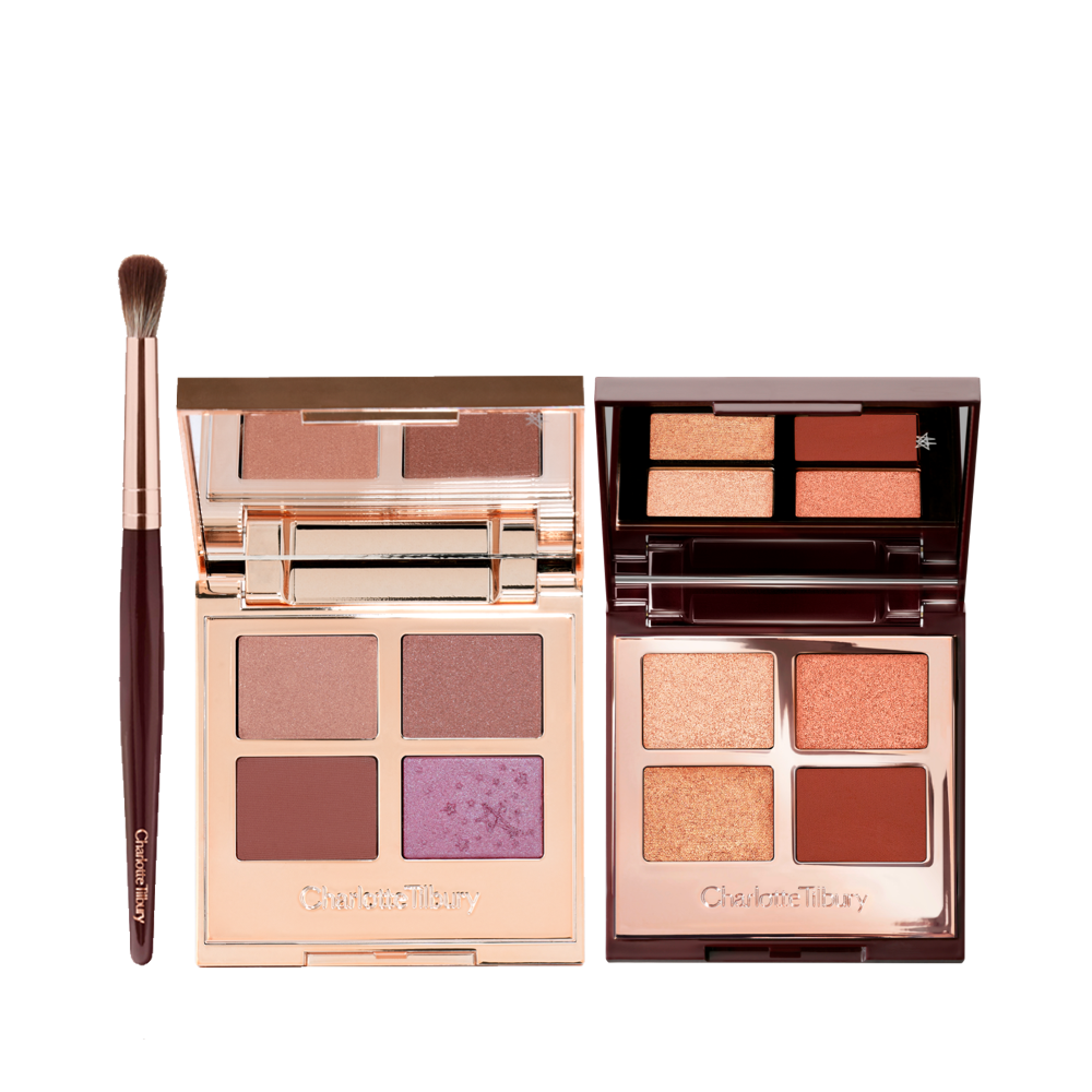 An eyeshadow blending brush and two, open quad eyeshadow palettes with mirrored lids, both with matte and shimmery eyeshadows in shades of nude beige, brown, mud brown, violet, champagne, peach, gold, and clay-brown.